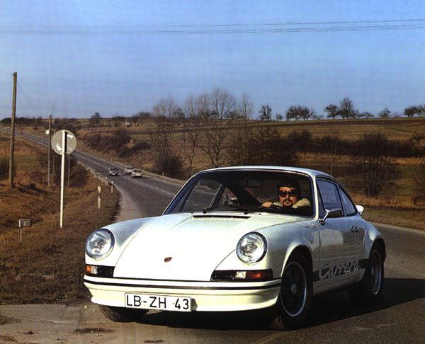 A German 1973 911 RS 2.7 with black striping. The driver is wearing matching clothes.